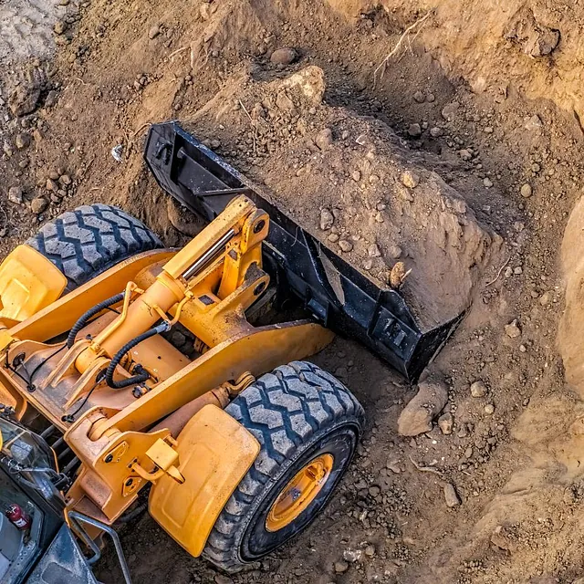 Gravemaskin sett ovenfra, fyller skuffen med jord i en dyp grop.